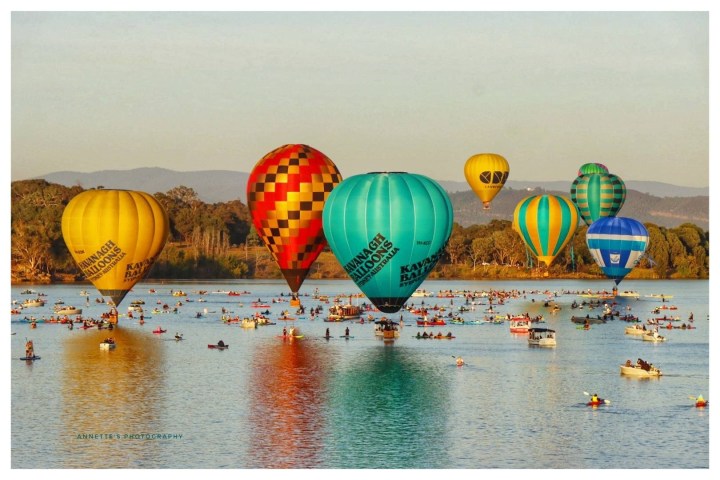 Colorful hot air balloons and boats on a lake during a relaxed, sunny day.