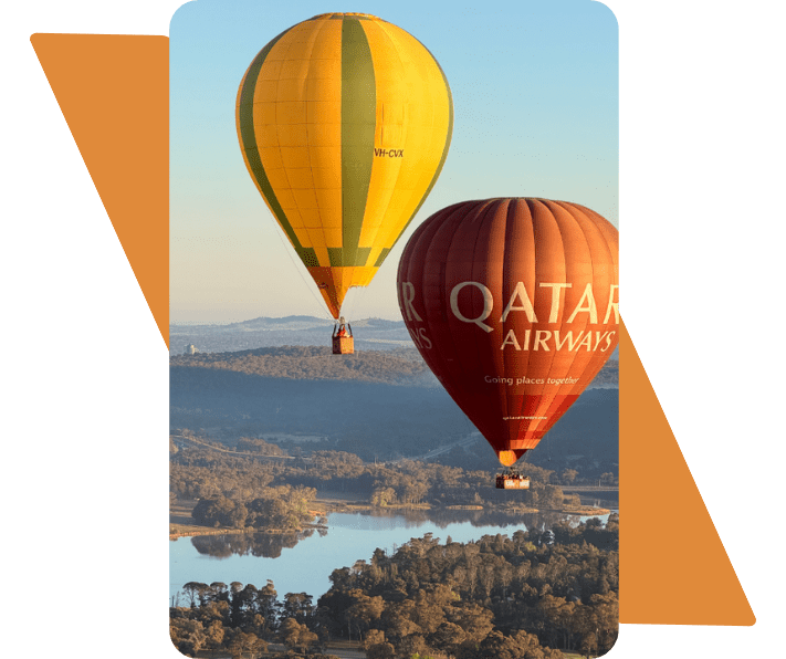 Two hot air balloons flying over a scenic landscape with trees and water.