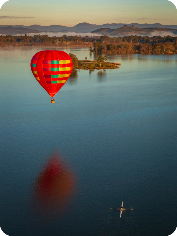 Colorful hot air balloon and kayaker on a calm lake with misty hills in the background.